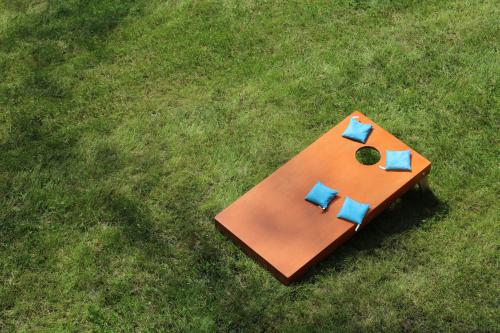 A wooden cornhole board sitting on the grass with 4 blue bags on the board.