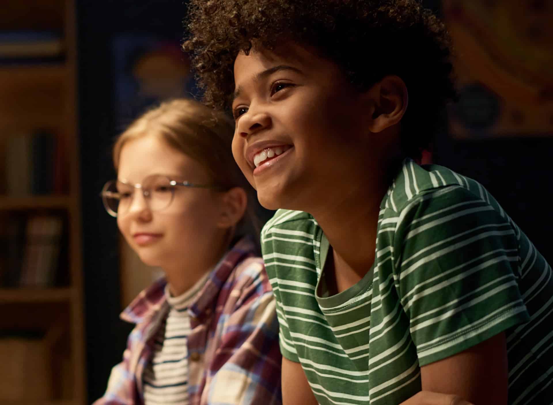 Two children smiling together in a dim room during a YMCA kids night out program