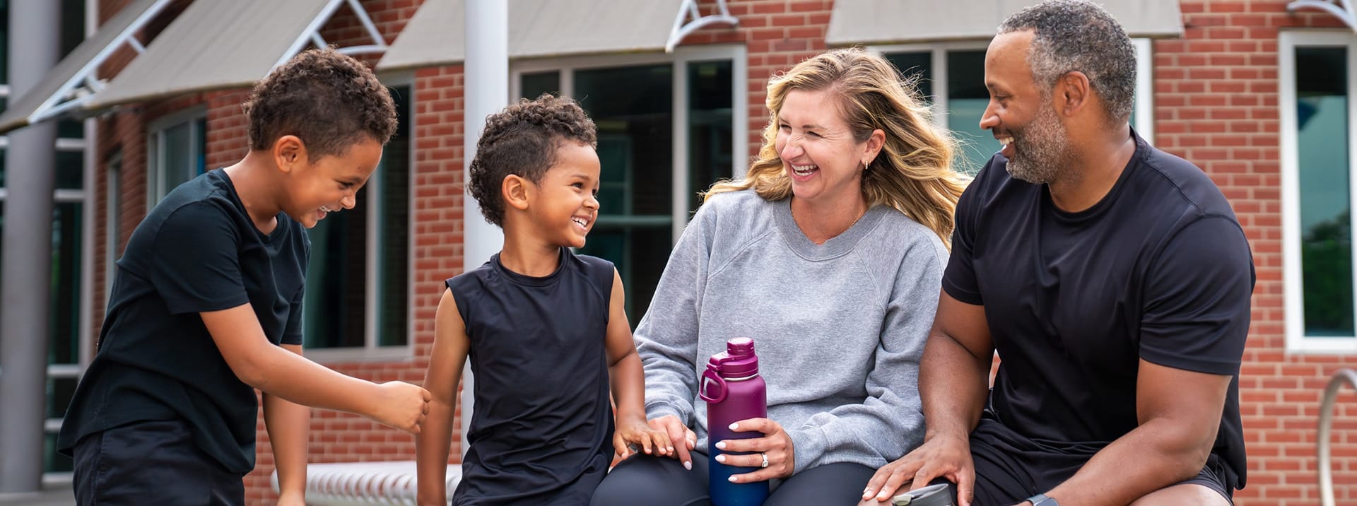 Family of four laughing together outside a YMCA building