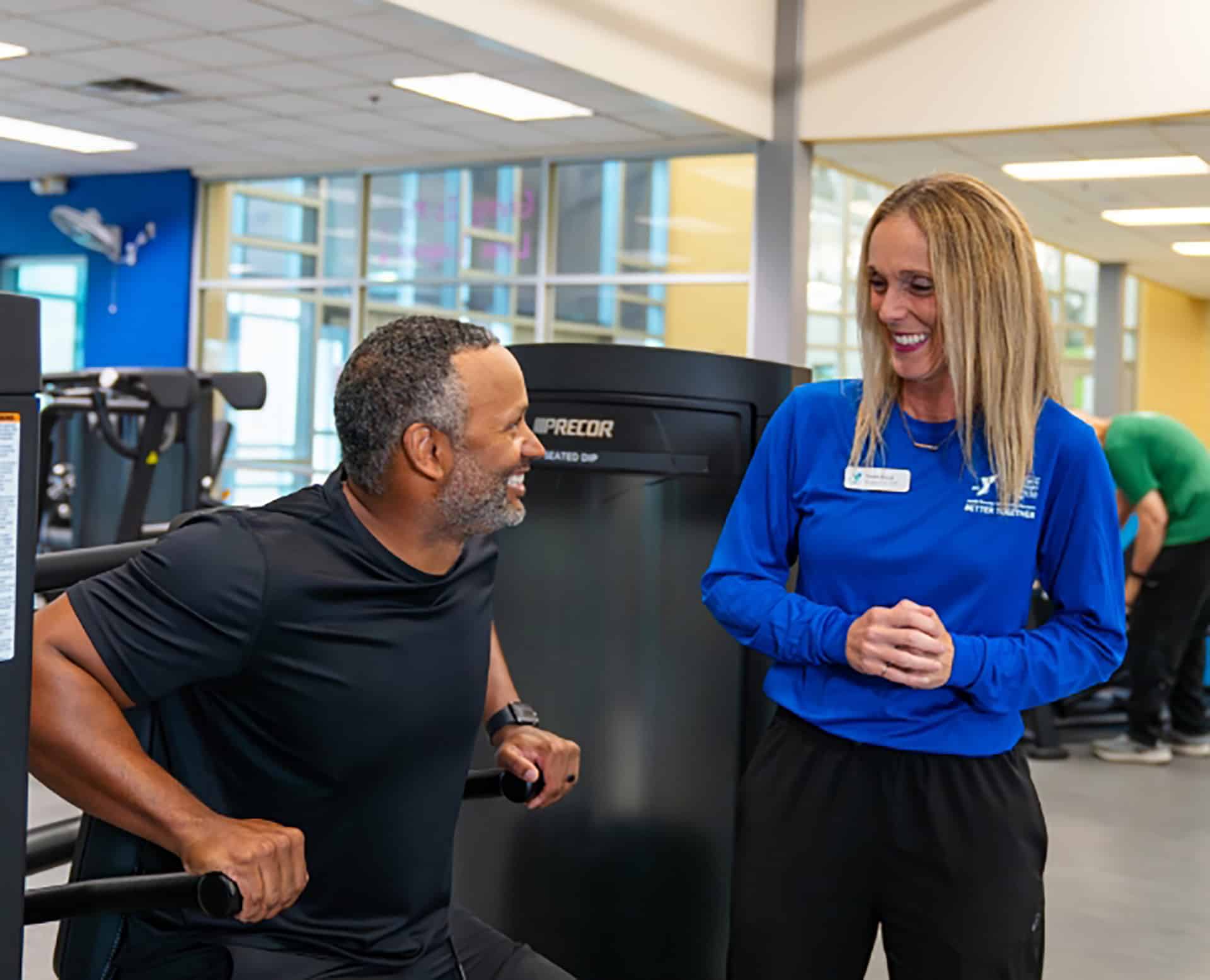 YMCA trainer coaching a member using a Precor strength machine in a fitness center