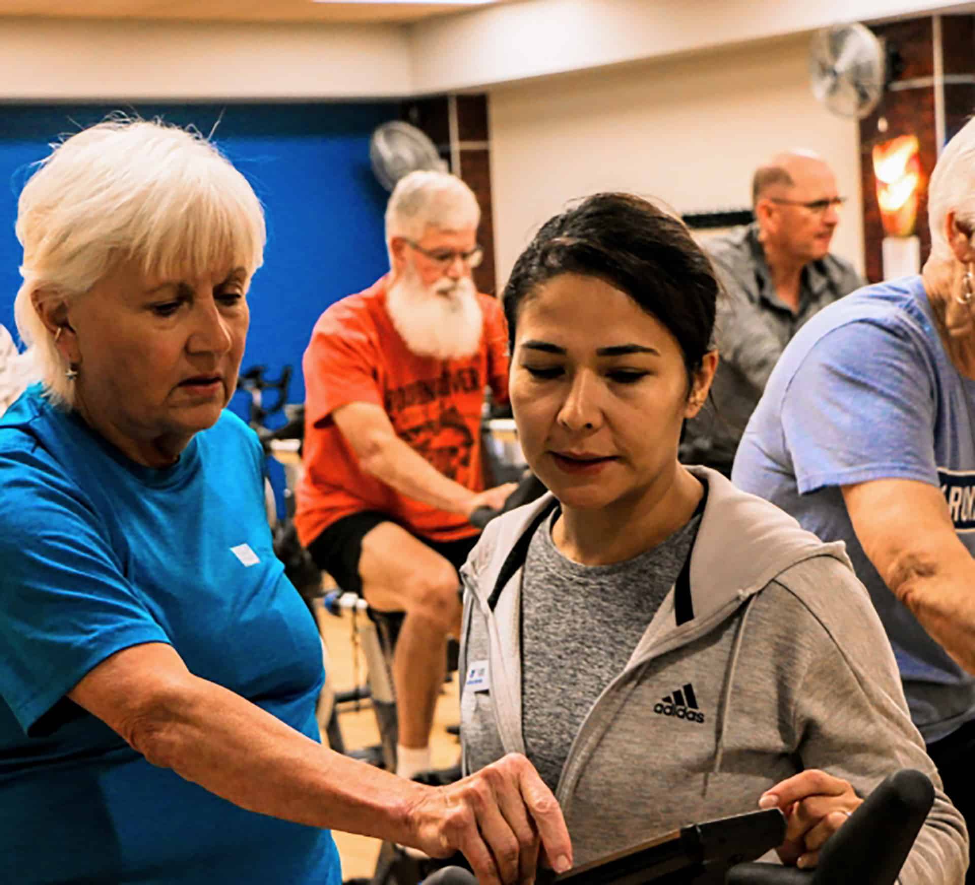 Older instructor guiding a woman through equipment during a YMCA group fitness cycling class