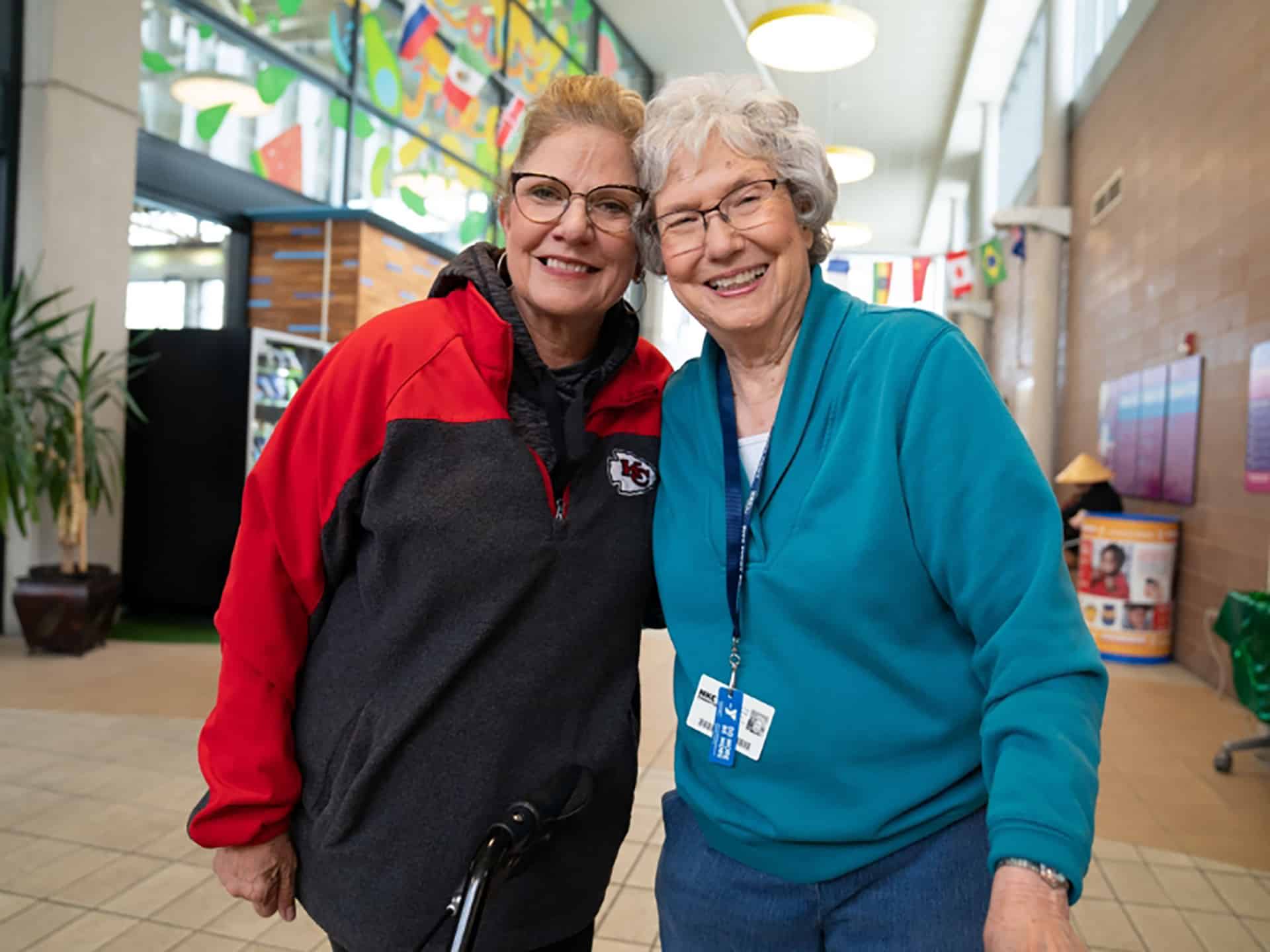 Two older women smiling and embracing in a bright YMCA lobby