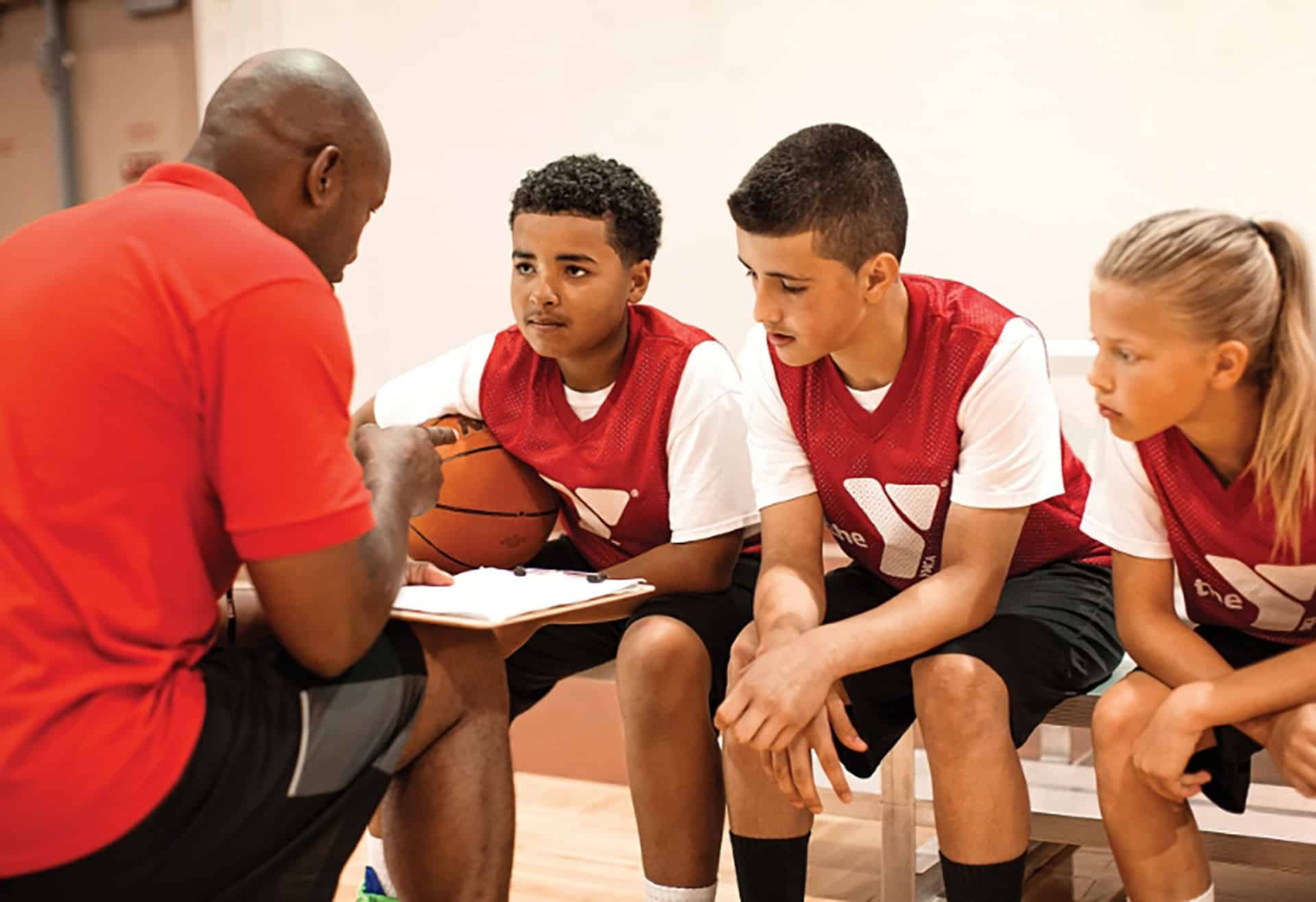 YMCA youth basketball coach talking with three young players on the bench during a game