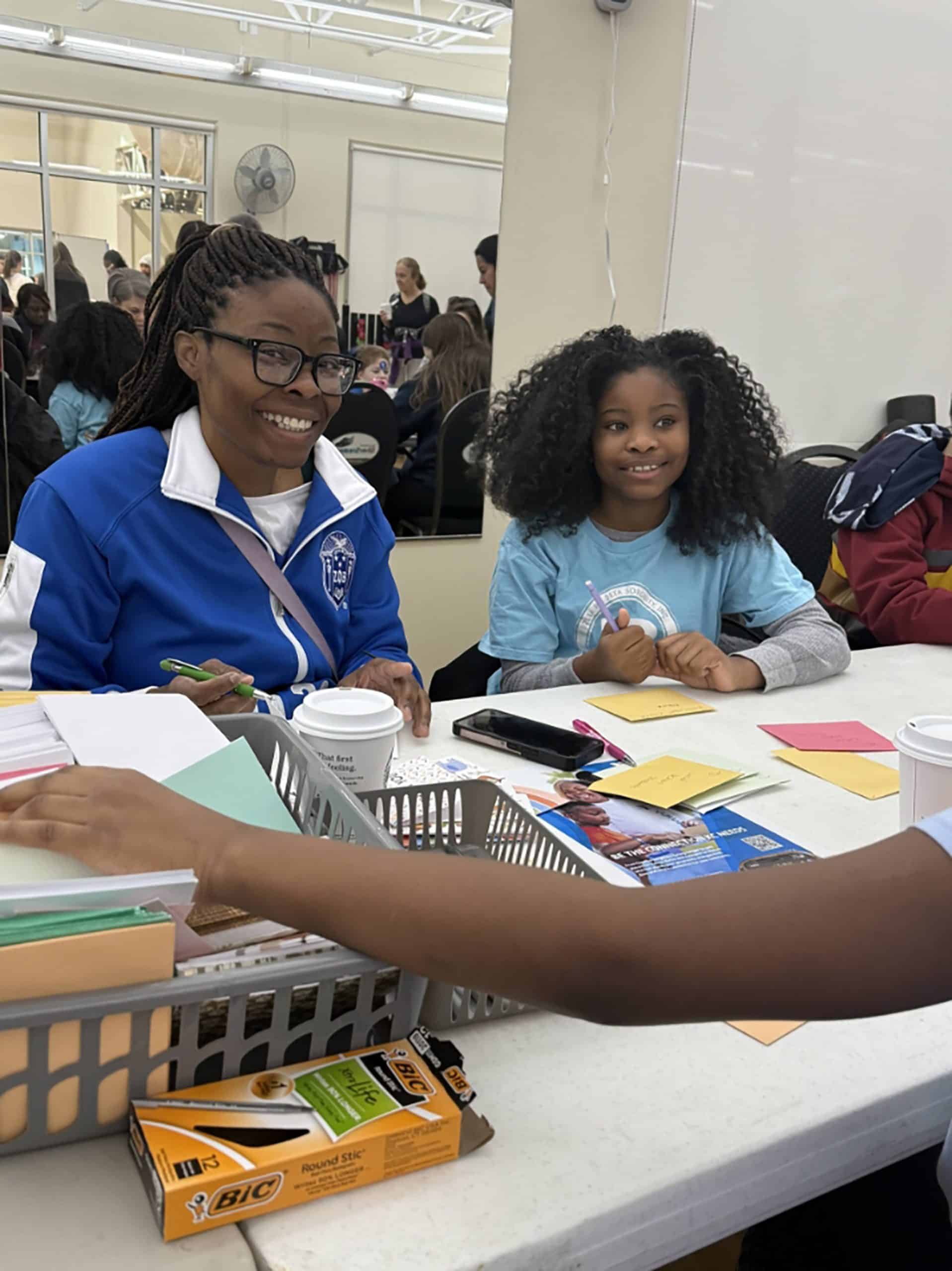 Volunteer and young girl smiling at a YMCA community event registration table