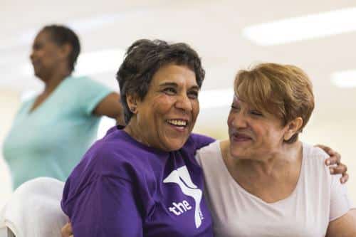 Two happy older women leaning into each other while sitting down
