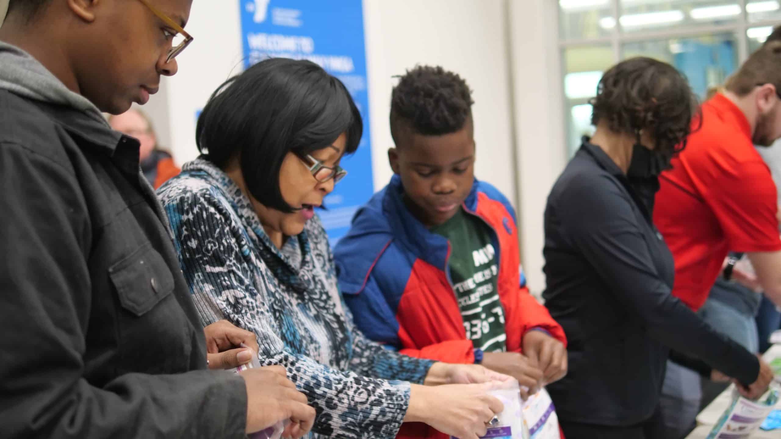 A family fills bags together at a welcome table inside a YMCA lobby
