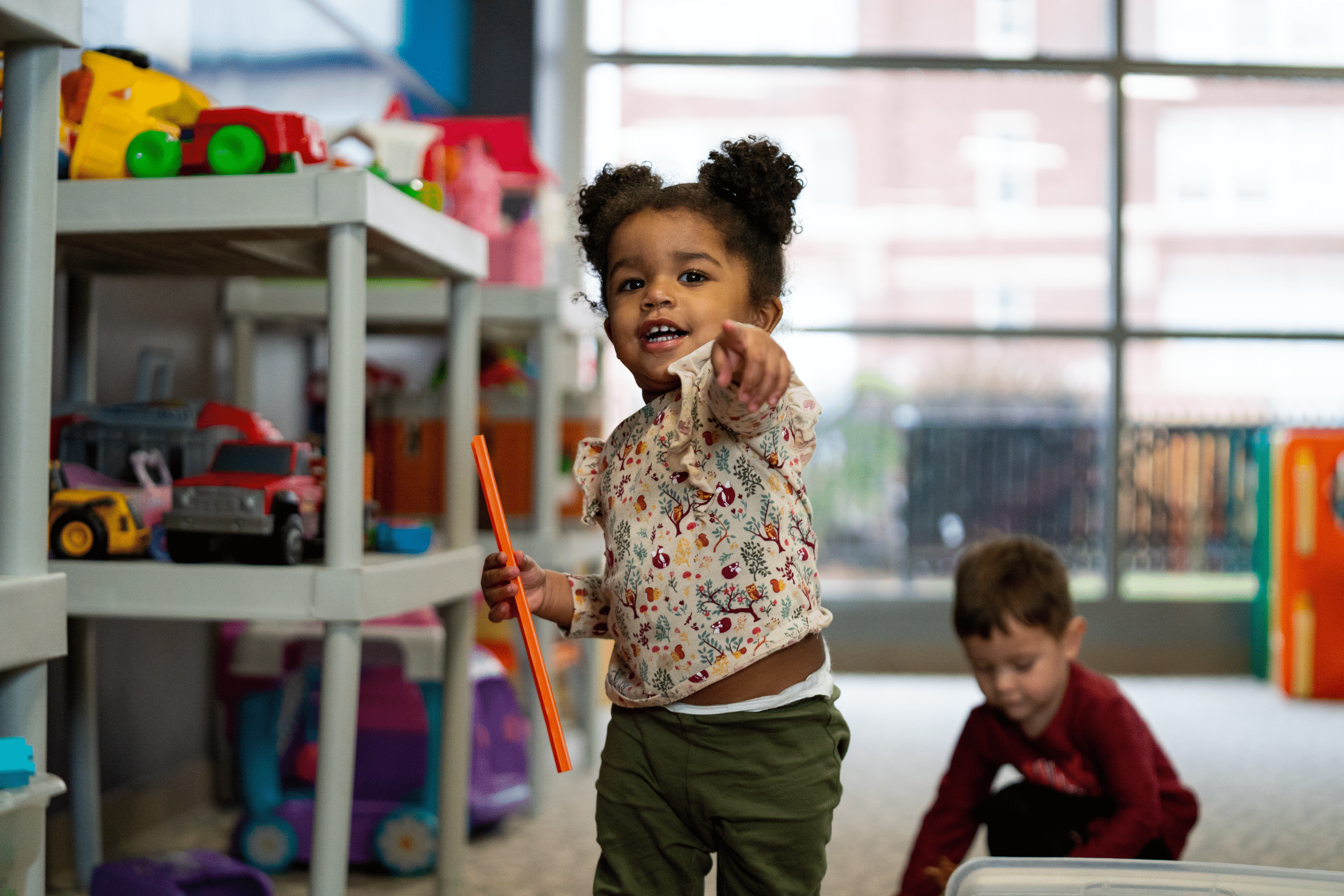 Young girl smiling and pointing while playing in a colorful child care play area