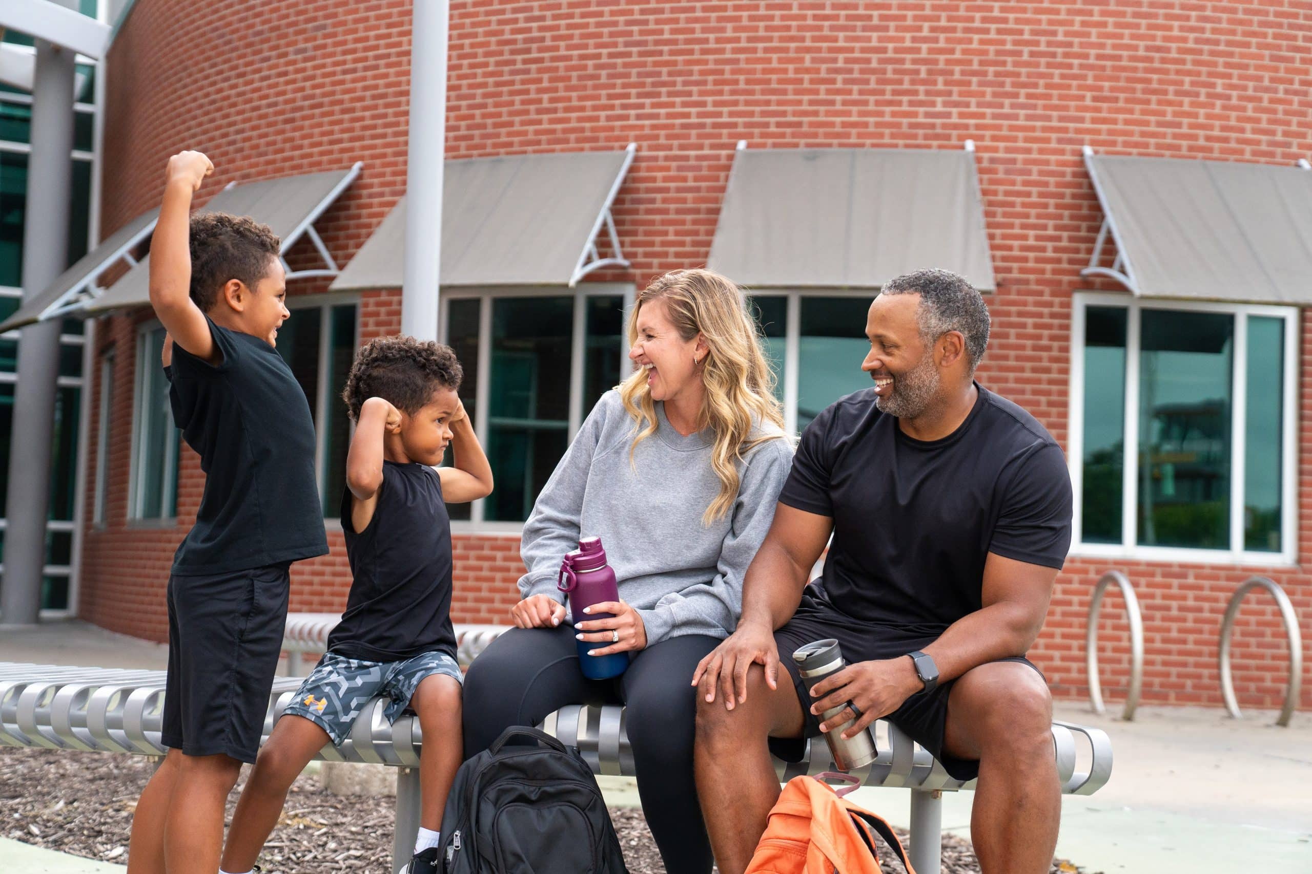 Parents and two young boys laughing together on a bench outside a YMCA center