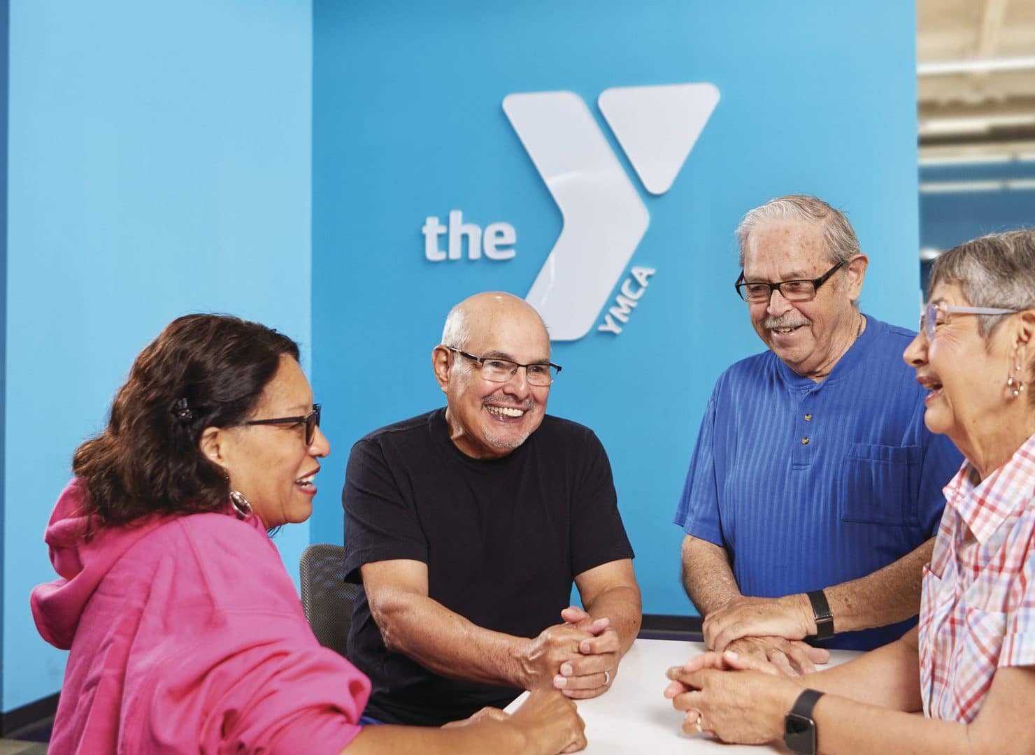 Four older adults talk and laugh at a lobby counter in front of a large blue YMCA logo wall