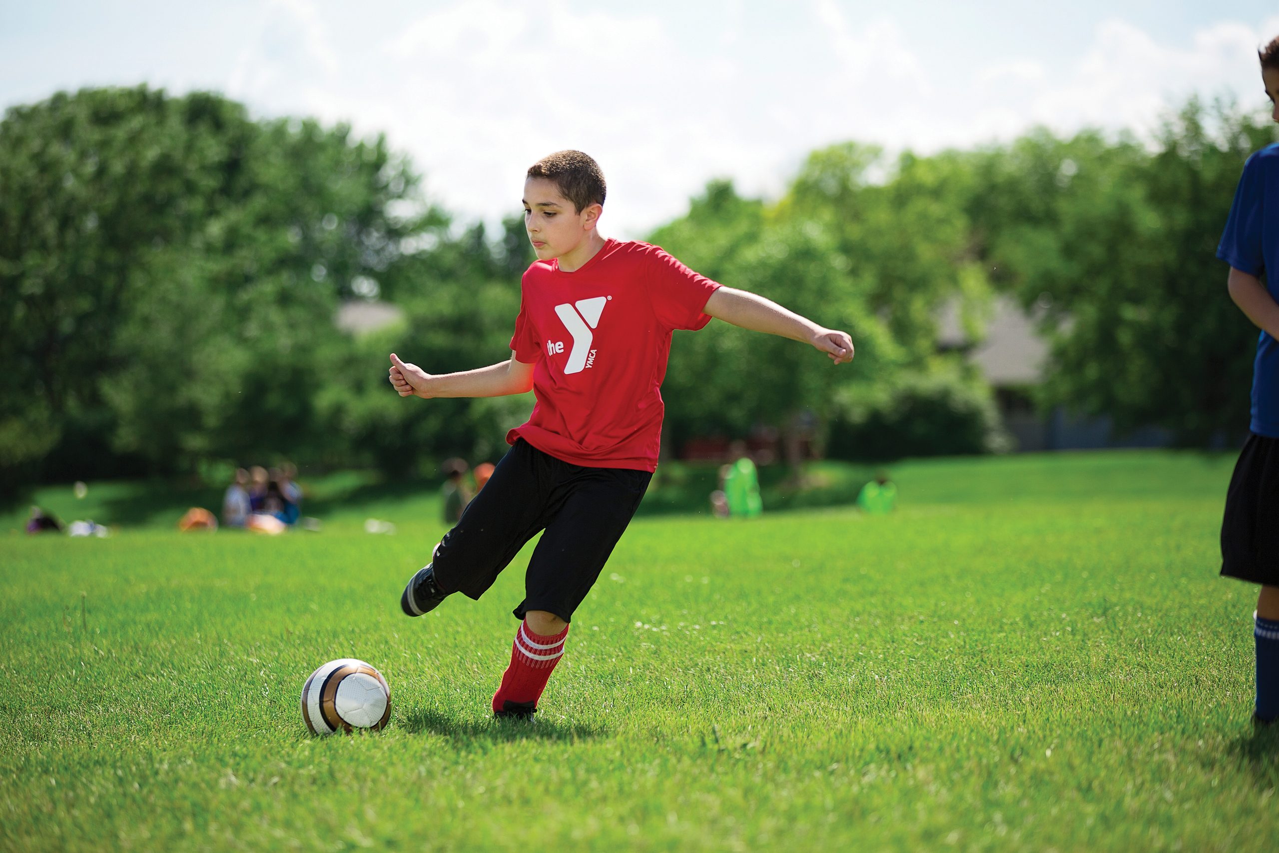 Young soccer player in a red Y shirt winding up to kick the ball on a sunlit grass field