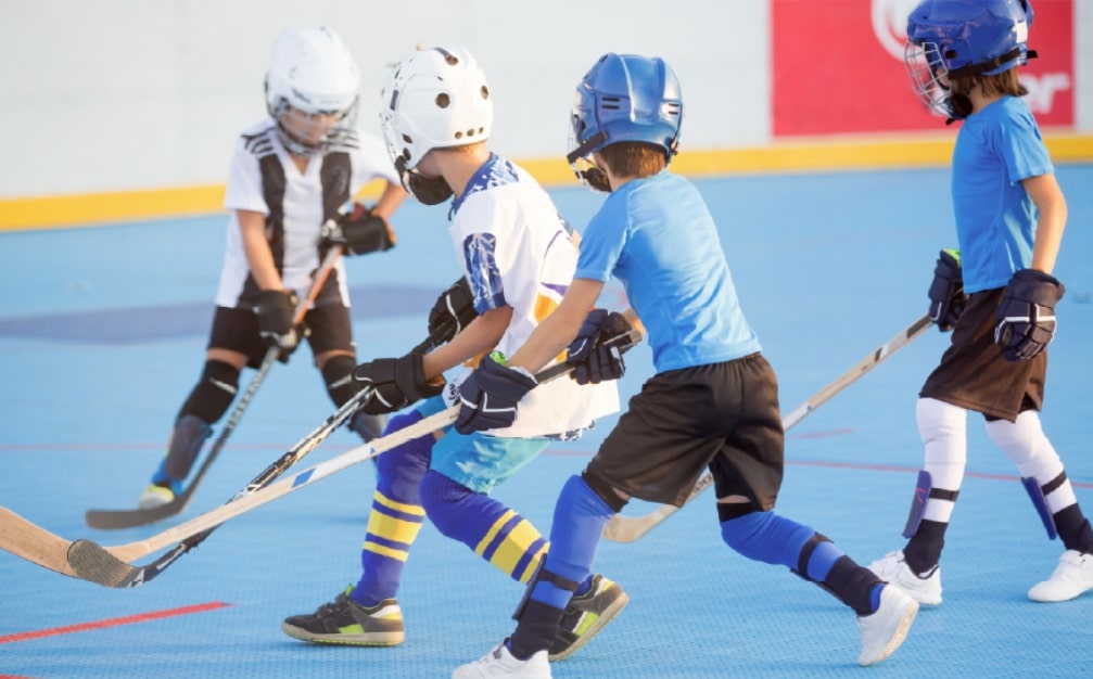 Kids in helmets and gloves playing street hockey on an outdoor sport court