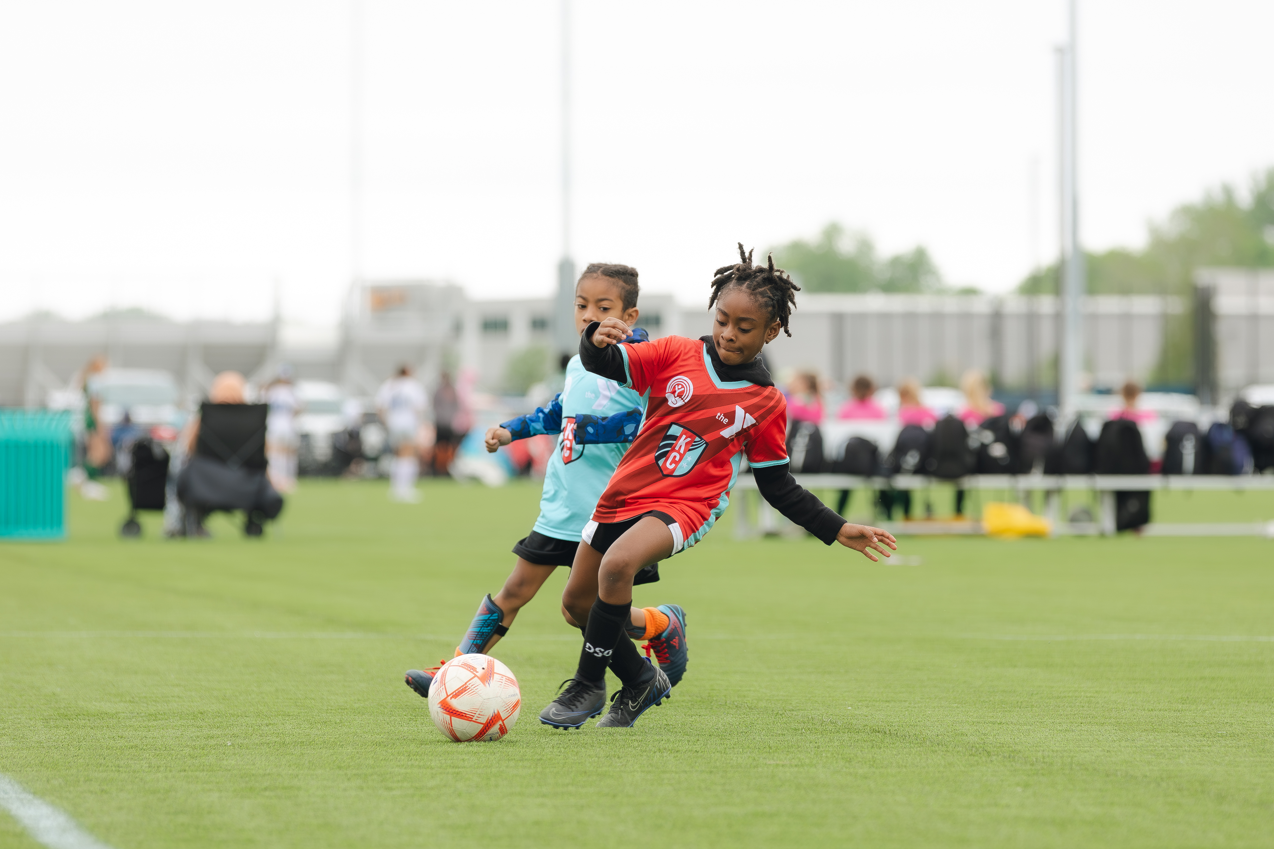 KC Current YMCA Youth Soccer player kicks ball, defender is in the background.