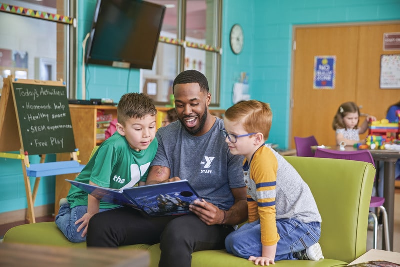 volunteer reads to two young boys in after school with y club academy