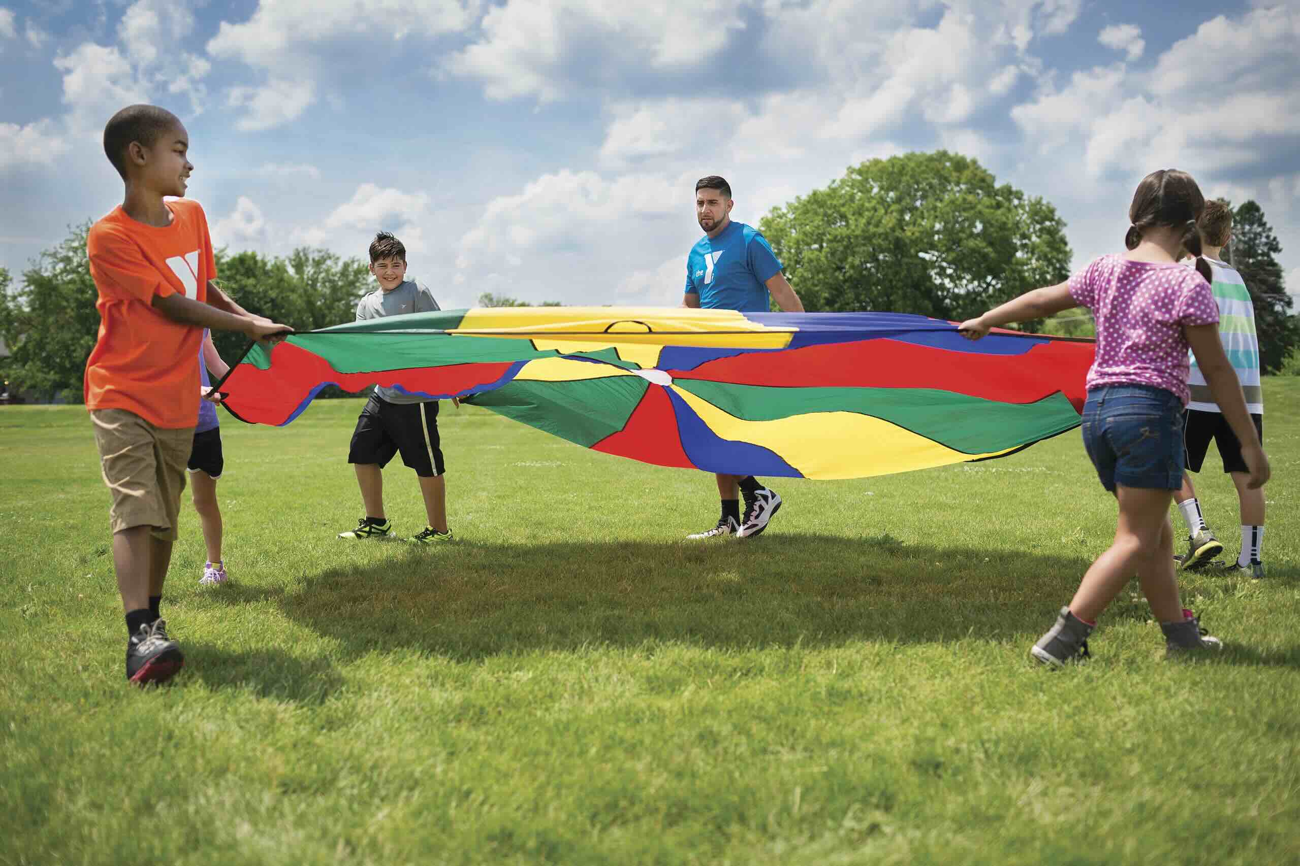 Four children play with a large parachute with a Y staff member.