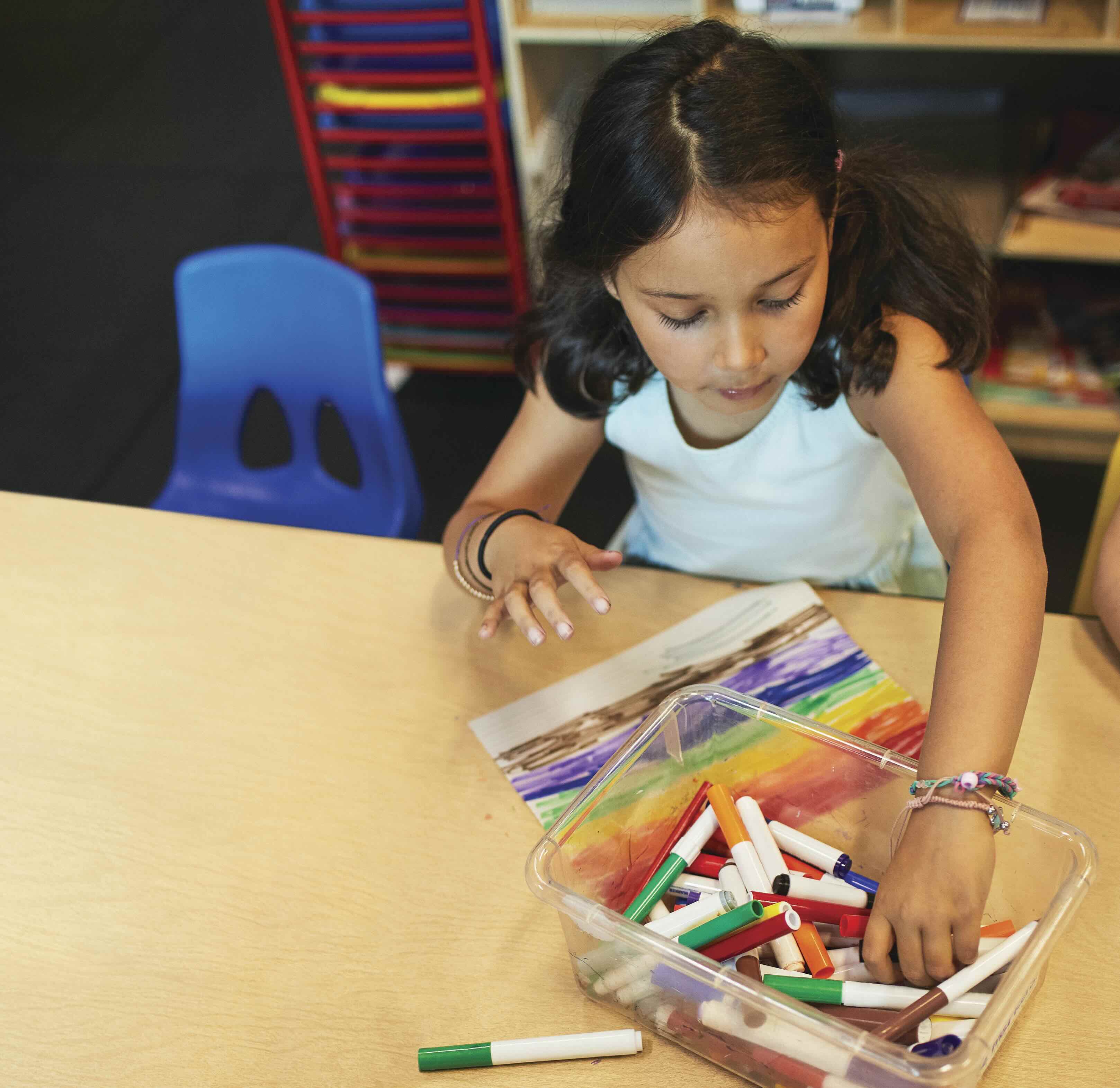 Two young girls sitting at a table coloring with markers.