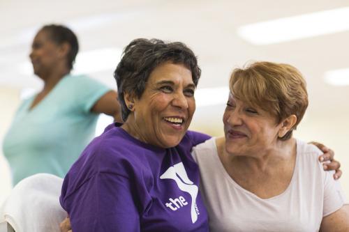 Two happy older women leaning into each other while sitting down 