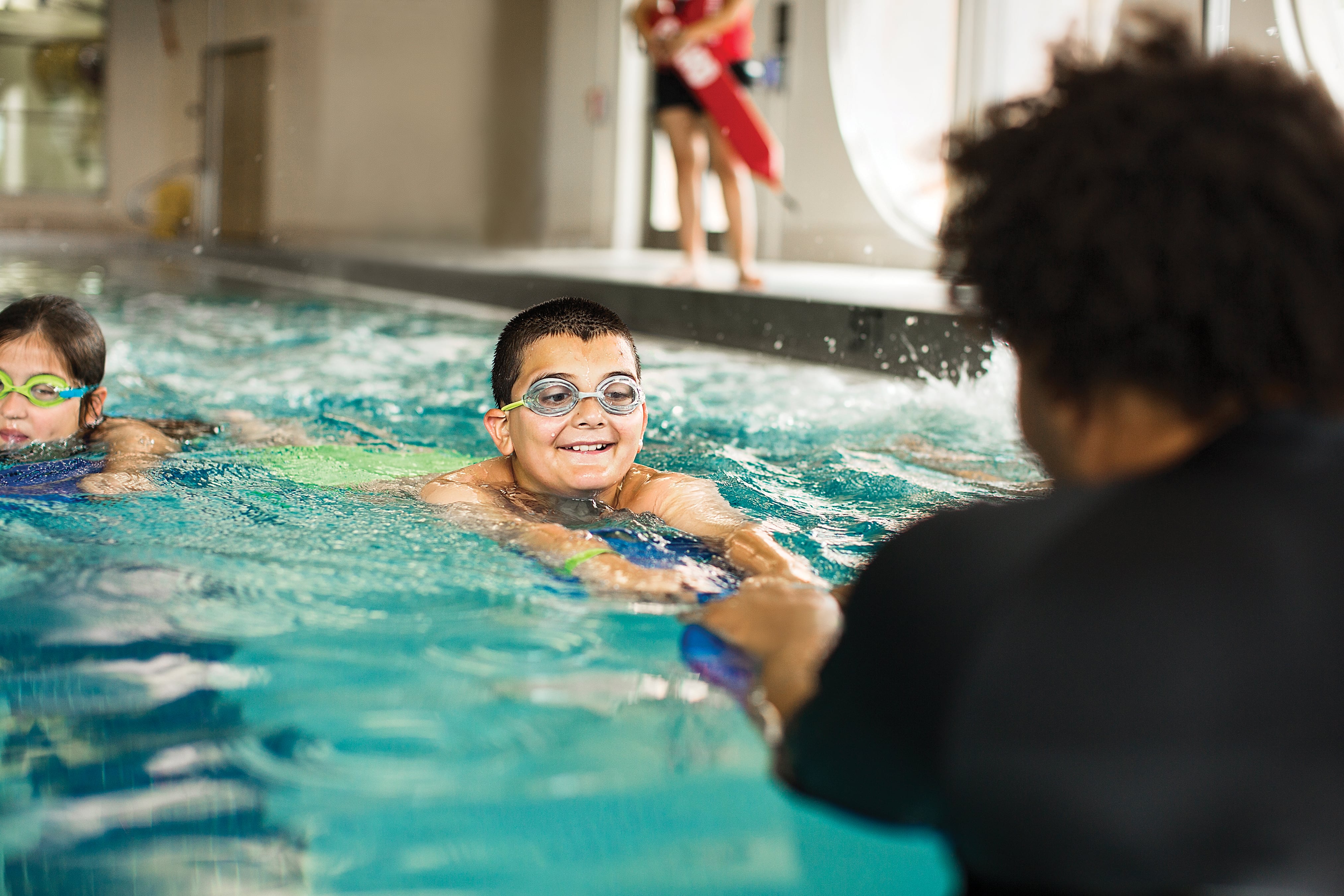 Young boy with goggles on swimming to instructor