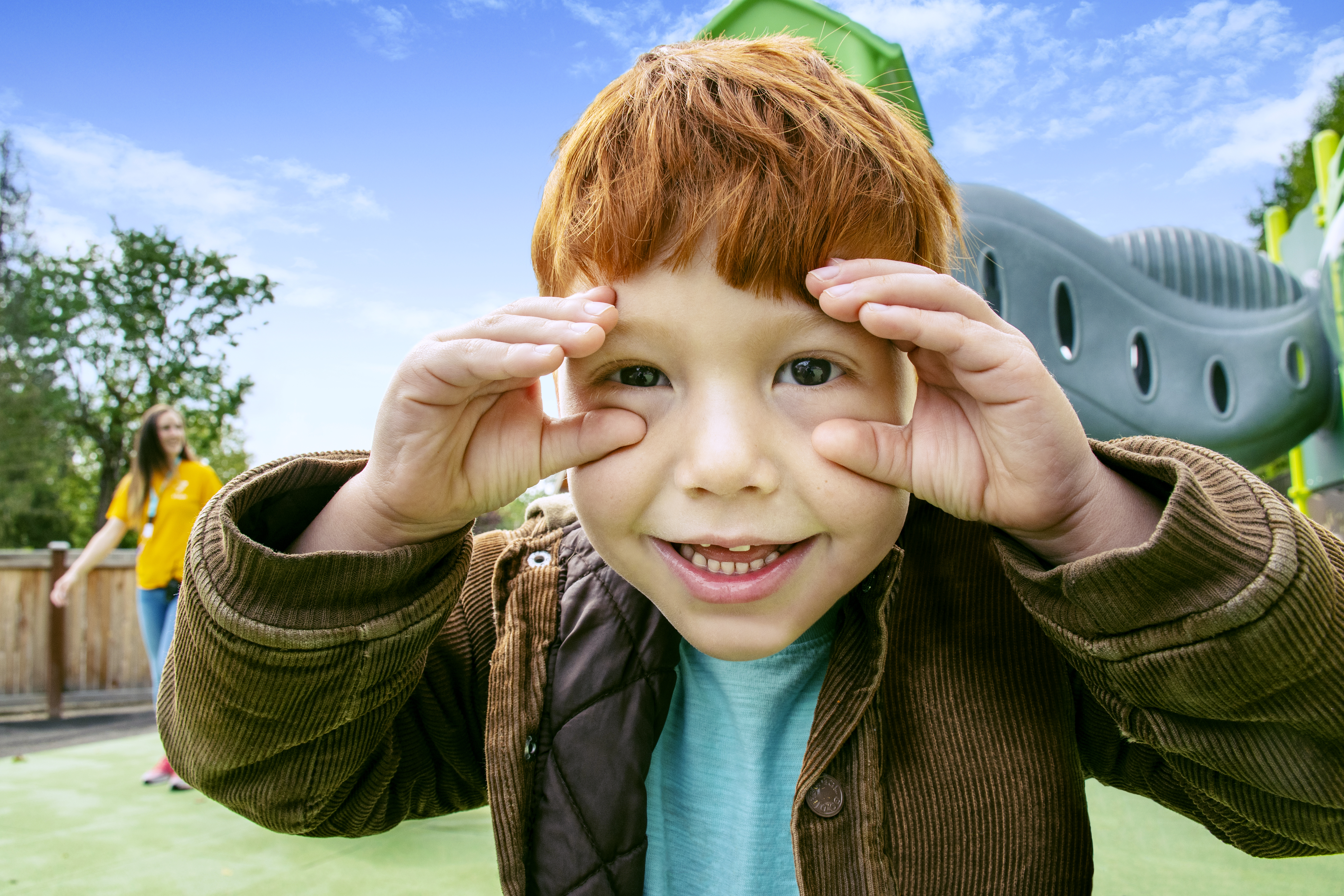 Child smiles at the camera with his hands around his eyes like he is using binoculars.