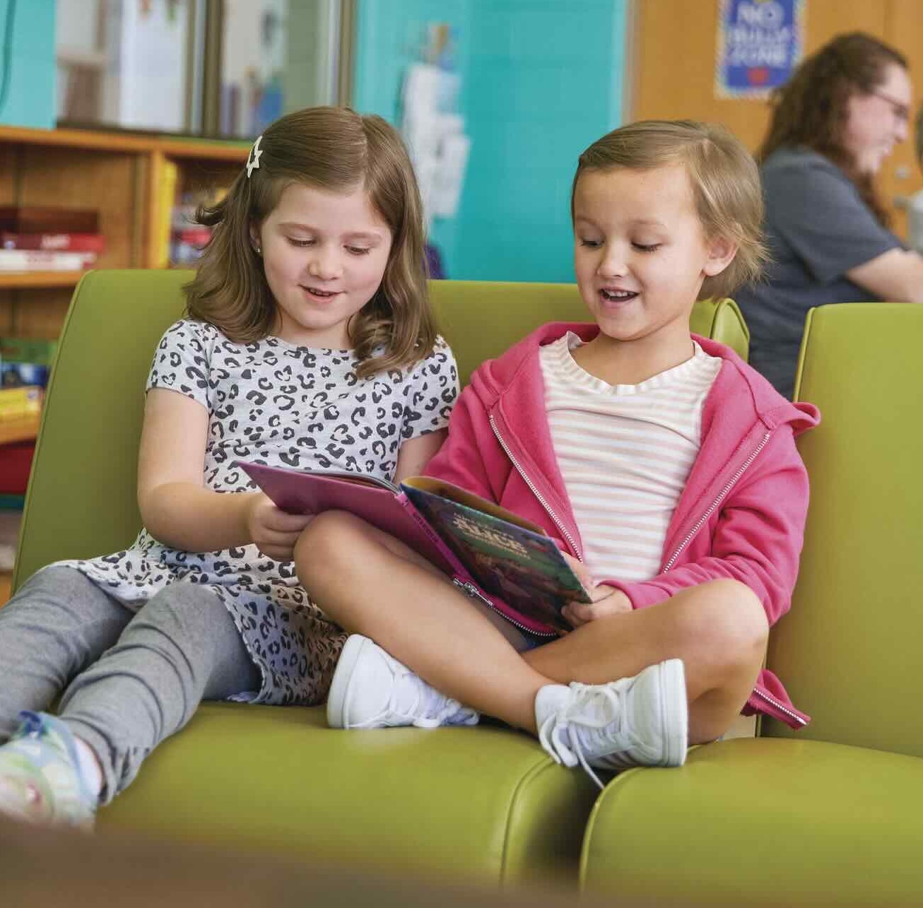 Two students sitting together reading a book.