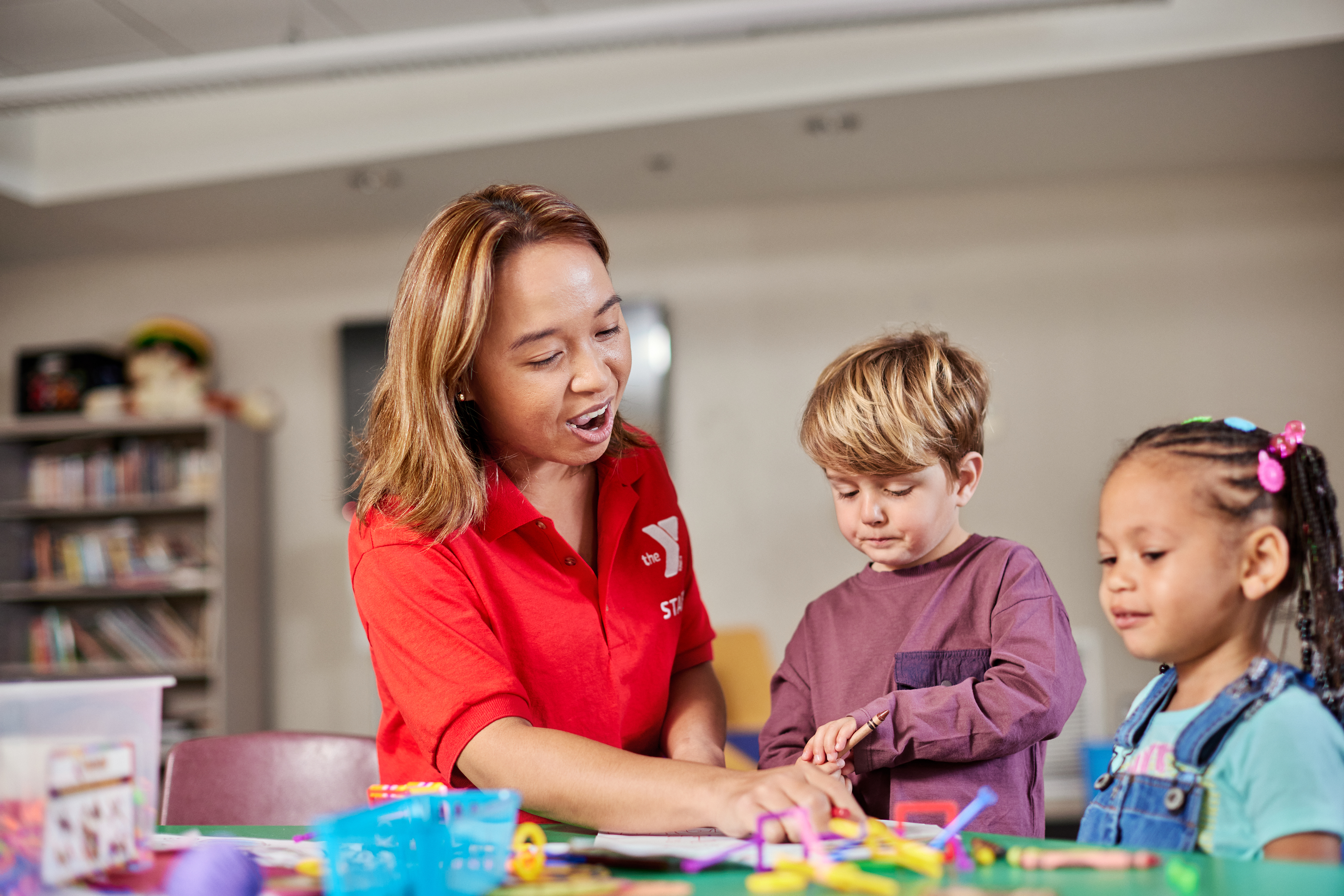 Staff member helps two students with activity at a table