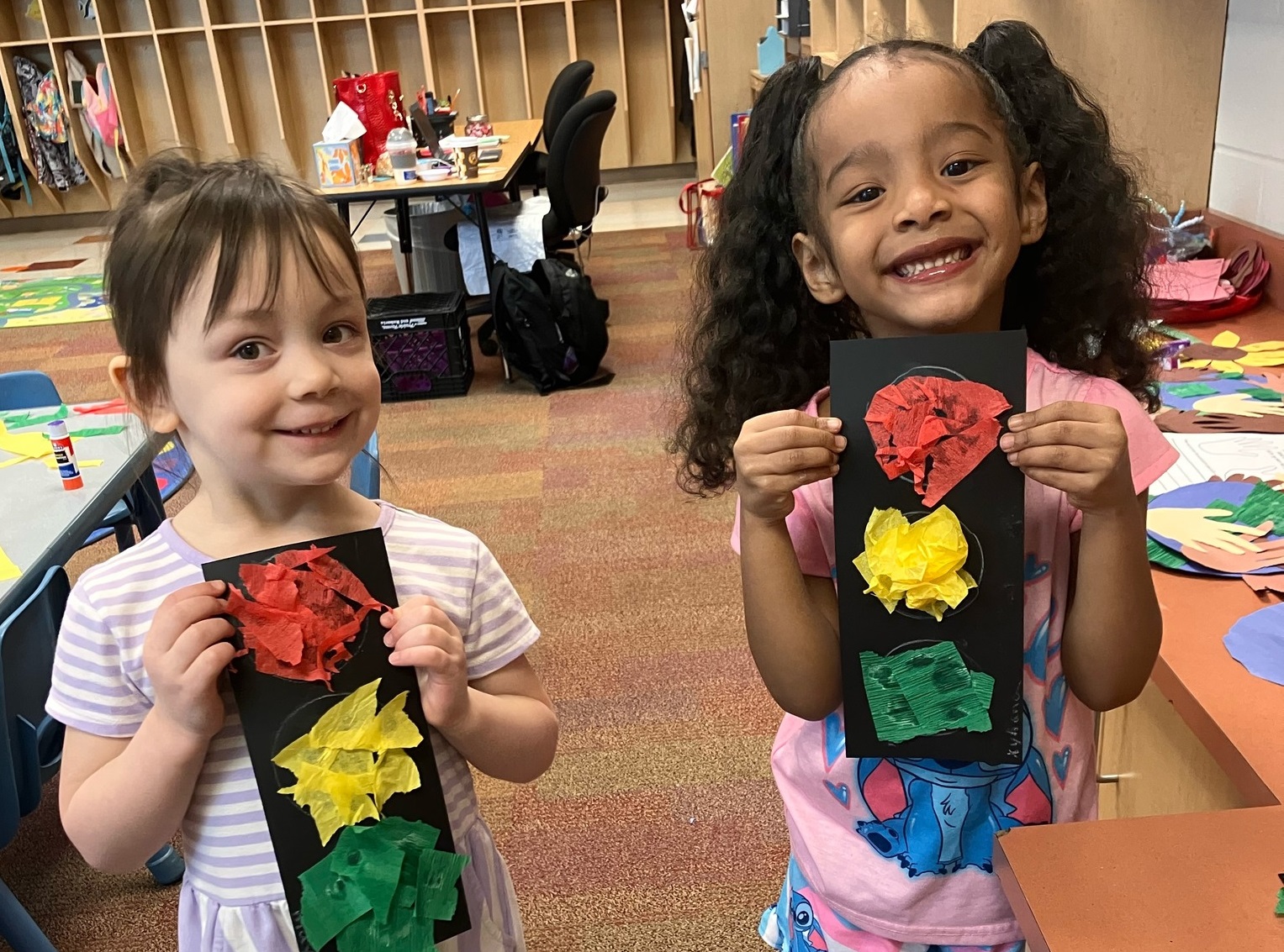 Photo of two girls, each holds an art project of a stop light