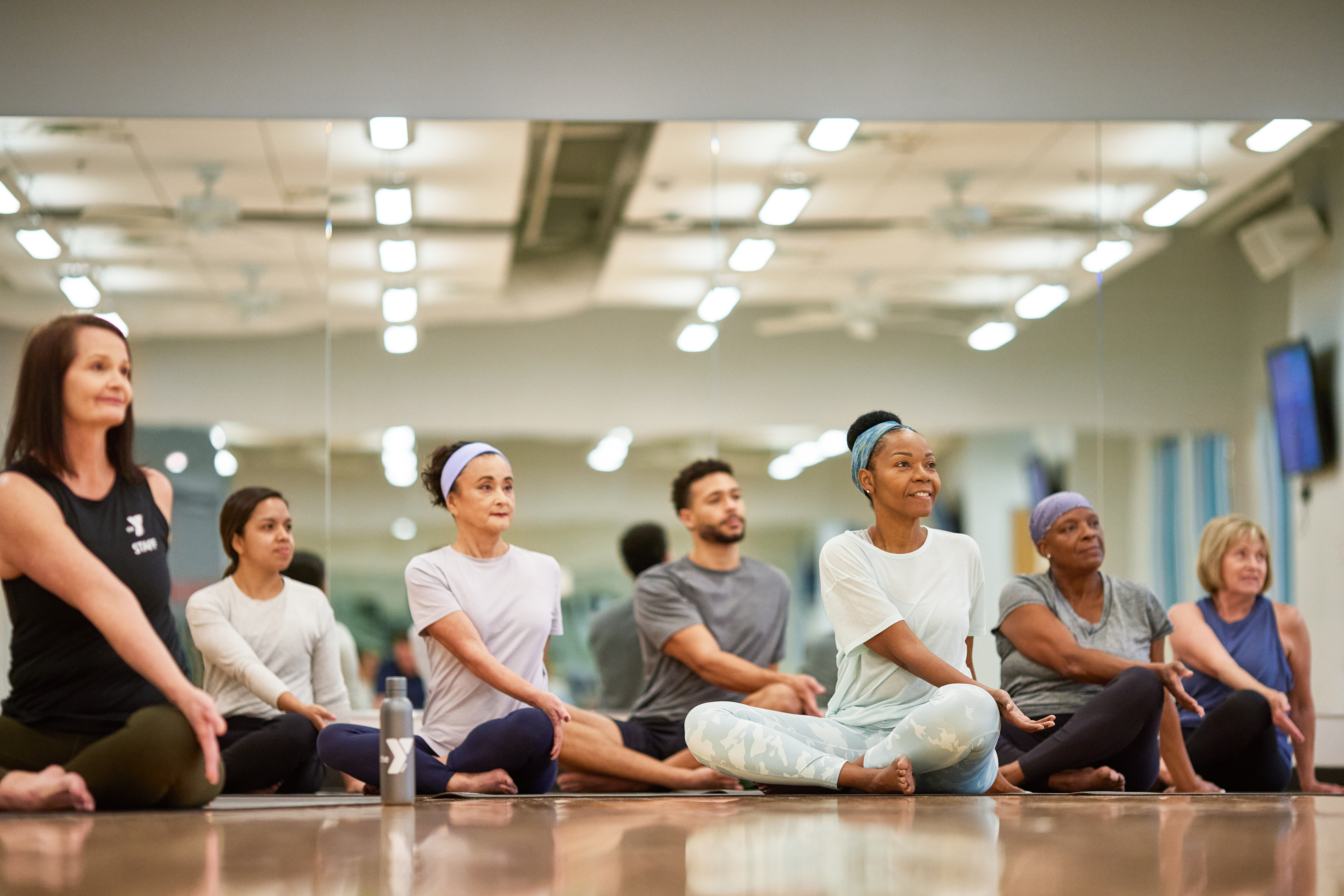 Photo of a group during a yoga class, they are sitting on the floor and stretching.