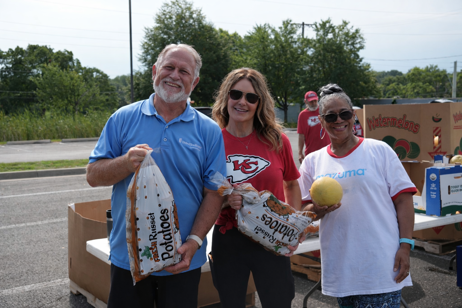 Volunteers posing with bags of potatoes and a cantaloupe while volunteering at a Cleaver food distribution events.