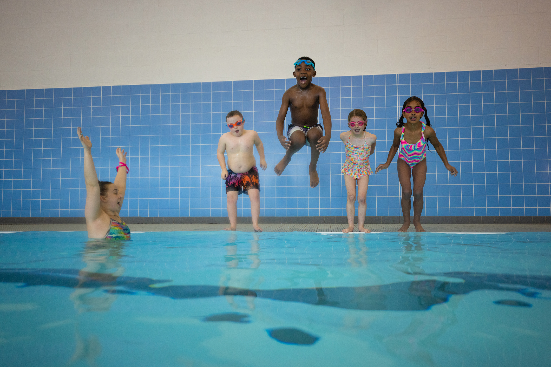 Indoor pool with children jumping in and instructor cheering