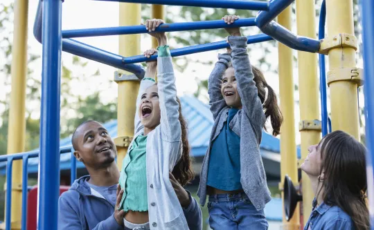 Children climbing on a jungle gym under the supervision of their guardian.