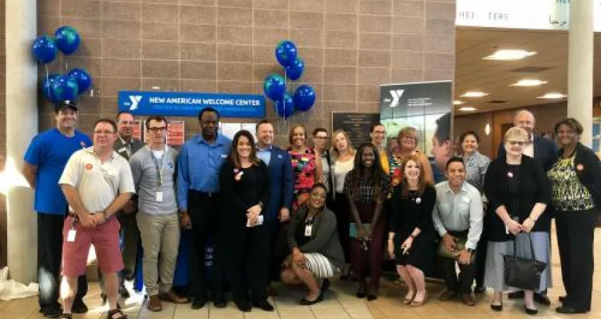 Event attendees and Y staff gather for a photo in front of the New American Welcome Center.