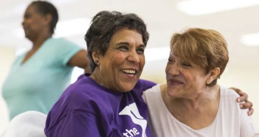 Two happy older women leaning into each other while sitting down 