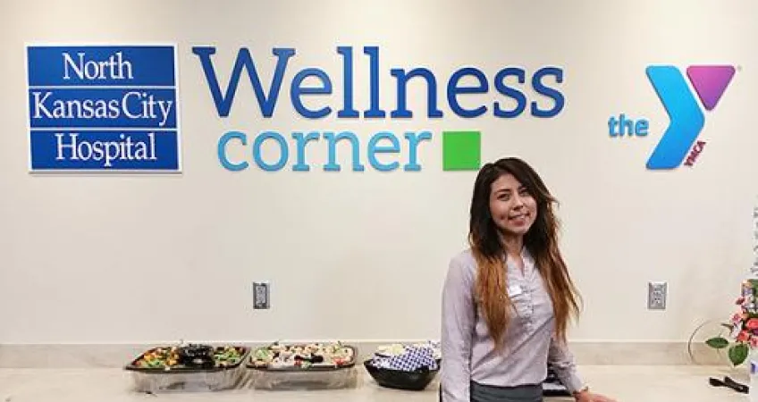 Young woman stands in front of the NKCH Wellness Corner sign at the North Kansas City Hospital 