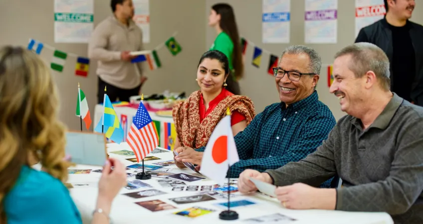 People of multiple nationality sit across from each other at a table covered in multiple countries' flags at a Kansas City YMCA.