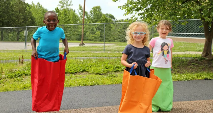 3 Children in the Head Start program jumping in jumping bags on the Kansas City YMCA playground.