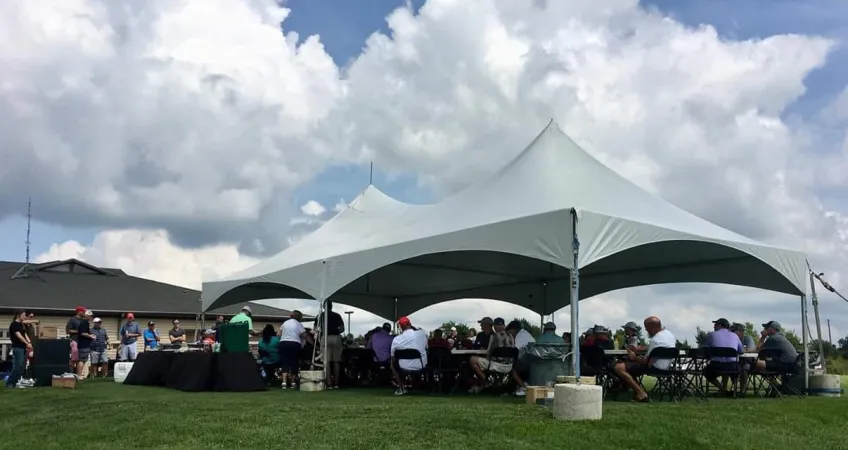 Large white tent with open sides shield golfers, seated at tables, from the sun at the Olathe Golf Tournament