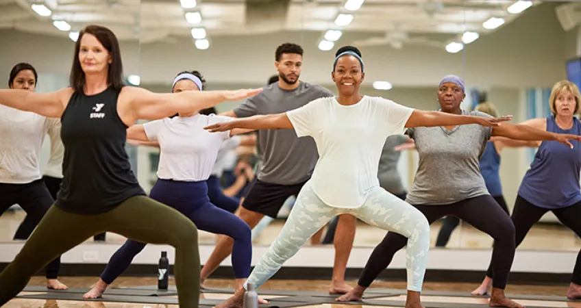 A group of YMCA members in the warrior 2 pose practicing yoga in a Kansas City YMCA group class.