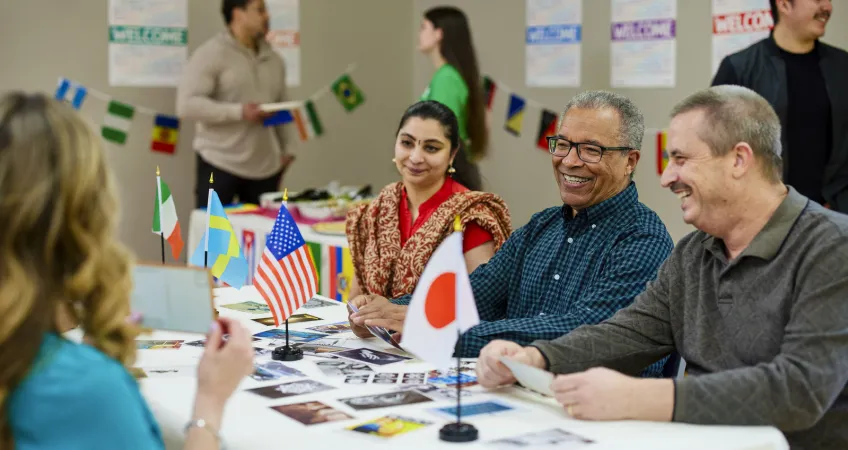 Three people sit at a table with photos and flags from different countries.