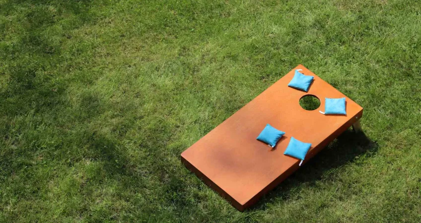 A wooden cornhole board sitting on the grass with 4 blue bags on the board.