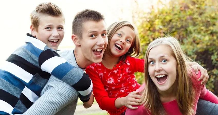 two babysitters outside giving a piggy back ride to the two kids they are watching.