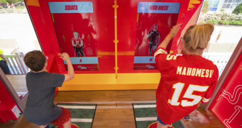 Woman in Mahomes Kansas City Chief's jersey and child working out in front of Chiefs Training Lab Powered by GEHA.