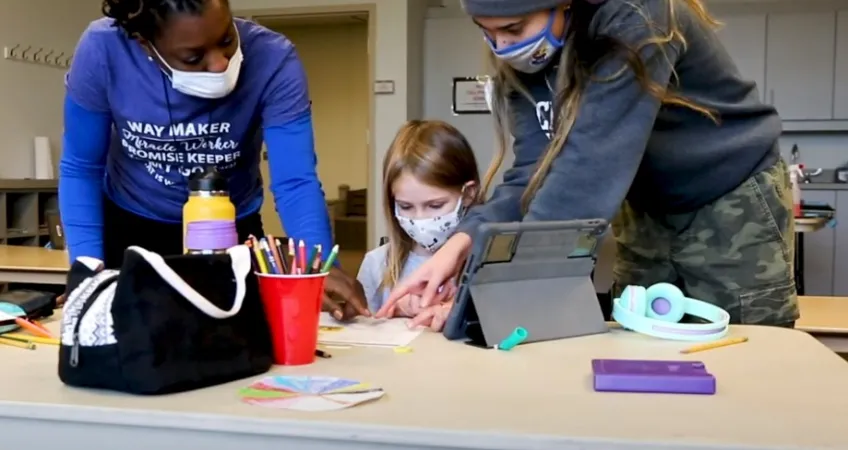 2 YMCA team members instructing a student on homework at a desk.