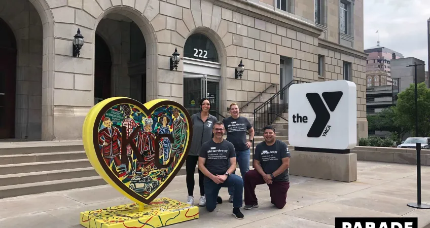 Four Y employees pose next to "Garments of Rabbitville" by Jacob Luke, a heart created for the Parade of Hearts event in 2024, located outside of the Kirk Family YMCA.