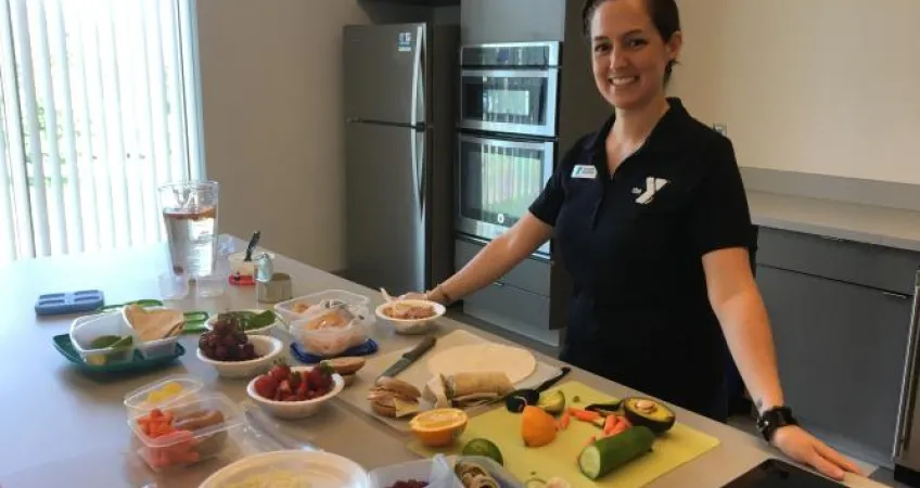 Greater Kansas City YMCA team member standing in front of a food prep table where fresh fruit and vegetables are being prepped.