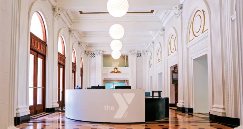 Photo of the lobby of the new Kirk Family YMCA. Shows restored lobby of the historic Lyric Theatre. In the center is the white welcome center desk with a Y logo on it.