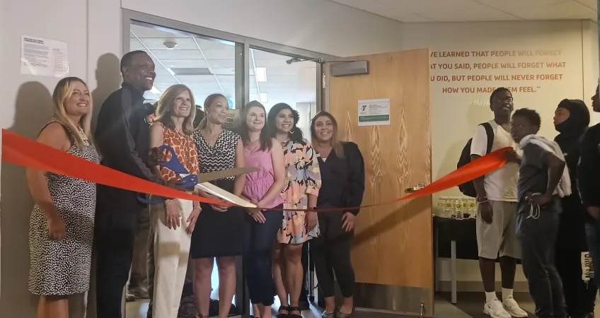 Staff and volunteers hold large ribbon and scissors in front of new teen tech center space at Linwood YMCA.