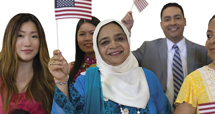 Group of people smiling while waving small American flags at naturalization ceremony.