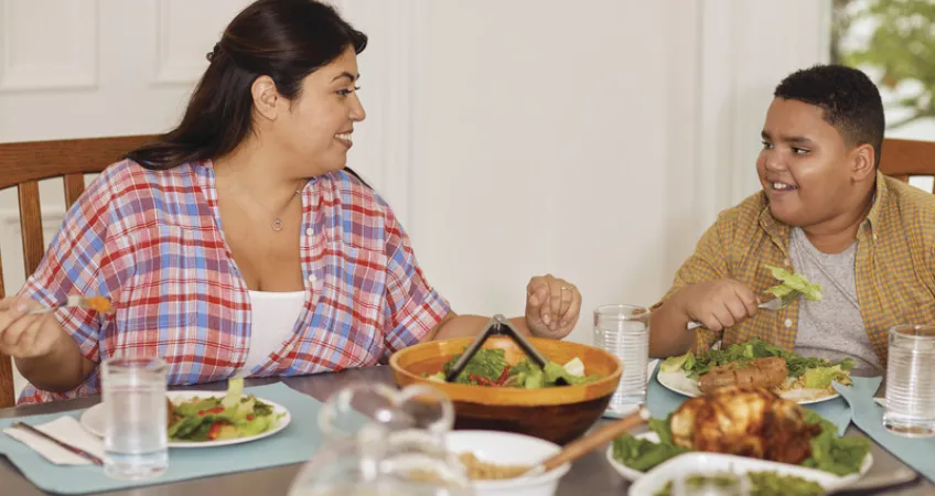 Mother and son sit at dinner table smiling as they eat a healthy meal.