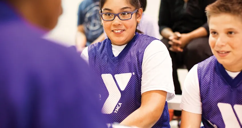 Two teen YMCA members talking with a YMCA coach.