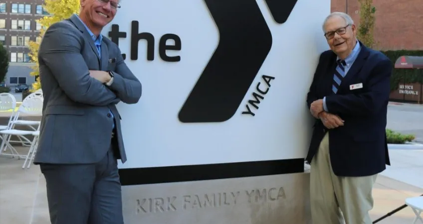 Photo of Mark Hulet and Frank Kirk in front of the Kirk Family YMCA sign.