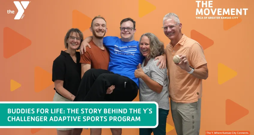 Five people huddle together to pose, while 2 people hold up the gentleman in the middle, everyone is smiling